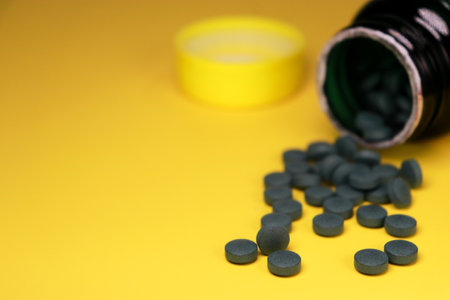 close up of green vitamin pills on yellow background with blurred bottle in backgroundの写真素材