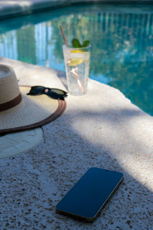 Refreshing glass of water, straw hat, sunglasses and phone off at the pool
