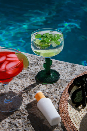 refreshing mojito cocktail at the pool with sunscreen, sunglasses and straw hat