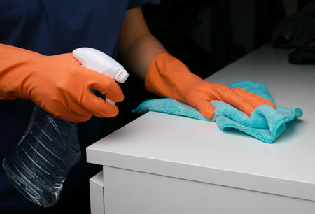 close up of womans hands in orange rubber gloves cleaning white dresser surfaceの写真素材