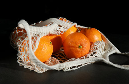 close up of fresh oranges in a mesh grocery bag, dark background