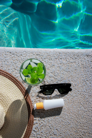 refreshing mojito cocktail at the pool with sunscreen, sunglasses and straw hat