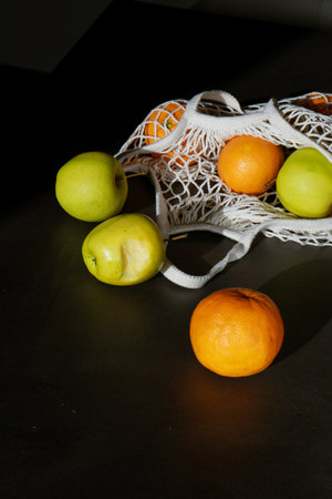 fresh green apples and oranges in cotton string bag on grey tableの写真素材