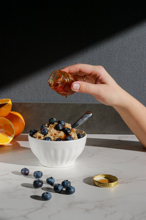 hand adding honey on oatmeal with blueberries on top in white porcelain bowlの写真素材