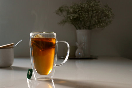black tea in a glas cup on white table, flower in background with copy spaceの写真素材