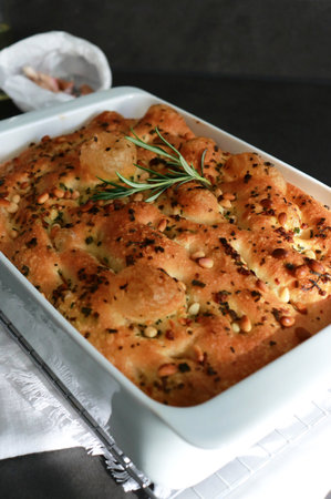 Italian garlic rosemary focaccia bread in white baking pan on grey table with sunlightの写真素材