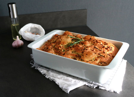 Italian garlic rosemary focaccia bread in white baking pan on grey table with sunlightの写真素材