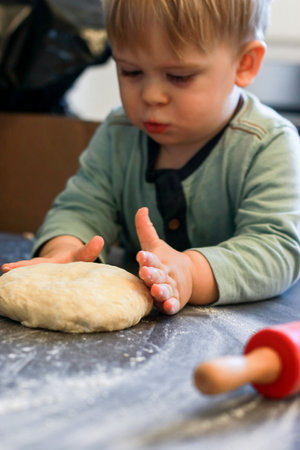 A little boy knead dough with a red rolling pin in the kitchenの写真素材