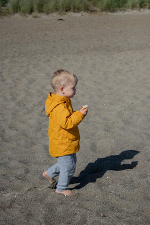 A little toddler walking on the beach wearing yellow jacket, cloudy weather with sunshineの写真素材