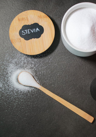 Natural stevia sweetener in a white bowl with a wooden spoon, grey marble table
