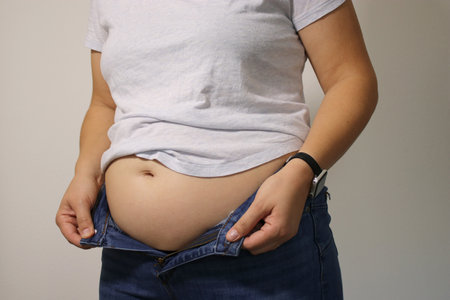 Close up of overweight young woman with fat belly after childbirth, pants doesn't fit