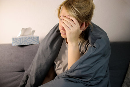 Sick caucasian woman with headache sitting on sofa with blanket at home