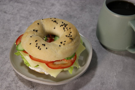 Top view of bagel with vegan cheese and fresh vegetables on a plate with cup of coffee, grey tableの写真素材