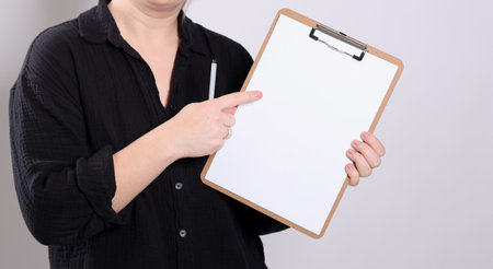Close up of a blonde young woman pointing on a blank mock up paper on a clipboardの写真素材
