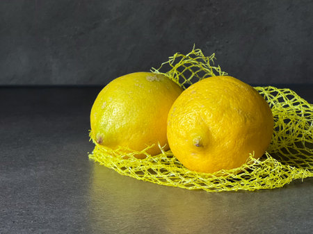 Close up of organic bio lemons on a yellow mash bag on grey table backgroundの写真素材