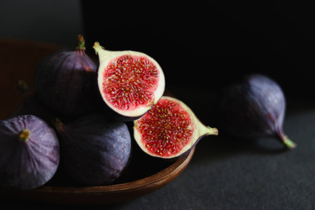 Close up of fresh ripe fig fruits in a wooden bowl on dark grey tableの写真素材