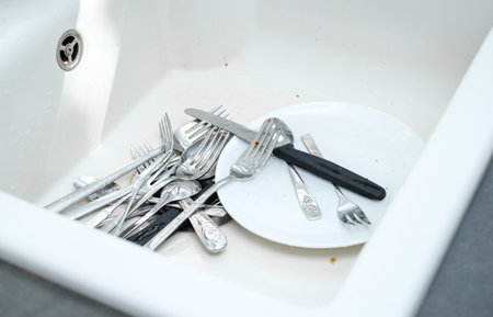 Close up of white ceramic kitchen sink full with dirty unwashed dishesの写真素材