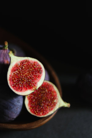 Close up of fresh ripe fig fruits in a wooden bowl on dark grey tableの写真素材