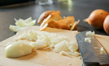 Close up of cutted white onion on a wooden board with a knife, grey kitchen table
