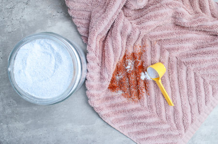 Close up of washing powder and a dirty pink towel with red stain on grey table. Cloth stain remover conceptの写真素材