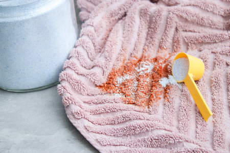 Close up of washing powder and a dirty pink towel with red stain on grey table. Cloth stain remover conceptの写真素材