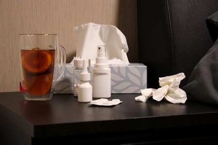 Hot tea with lemon, pills, nose spray, throat spray and on a night table near bedの写真素材