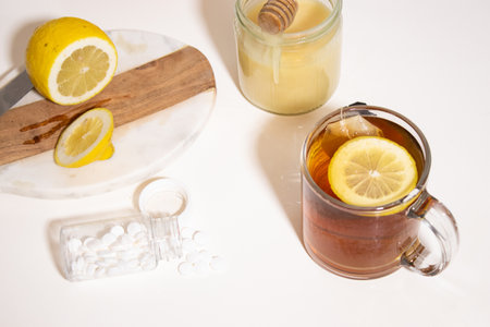 Hot tea with fresh lemon and honey, a bottle with white pills on white tableの写真素材