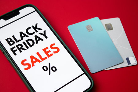 Close up of a smartphone screen displaying a Black Friday online sale on red background with credit cards and moneyの写真素材
