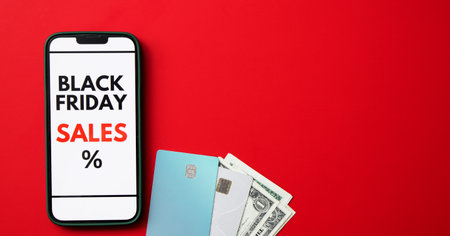 Top view of a smartphone screen displaying a Black Friday online sale on red background with credit cards and moneyの写真素材