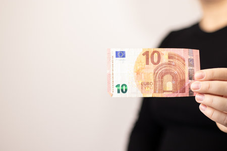 Close up of a woman holding one ten euro bill, grey backgroundの写真素材