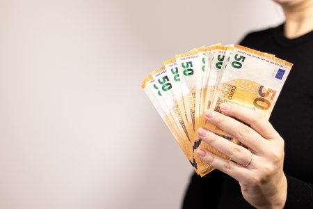 Close up of a woman holding fifty euro bills, grey background
