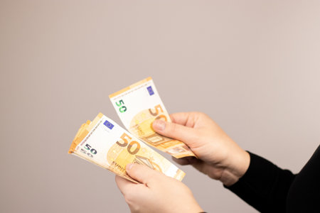 Close up of a woman counting fifty euro bills, grey backgroundの写真素材