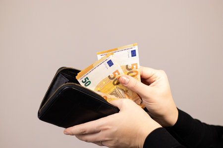Close up of a woman putting fifty euro bills in her wallet, grey backgroundの写真素材