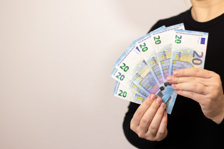 Close up of a woman holding twenty euro bills, grey background