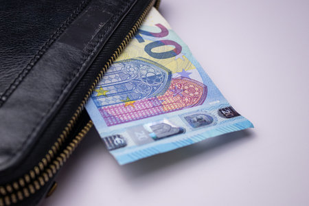 Black leather wallet with twenty euro bills banknotes on white background