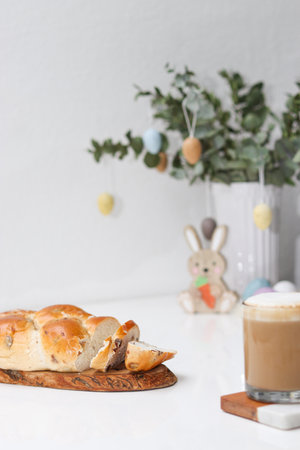 Cutted easter loaf bread on wooden plate on white table, blurry background with easter decoration