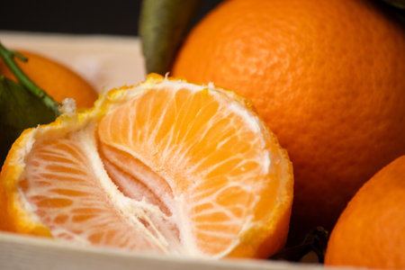 Close up of whole mandarines and one peeled fruit in a wooden box on grey table backgroundの写真素材