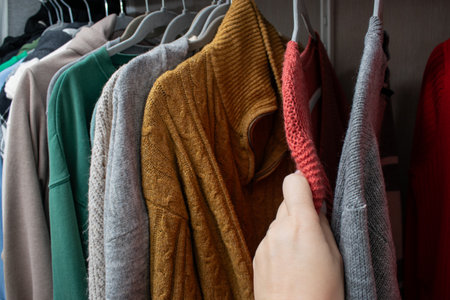 Close up of female hand choosing a warm knitted sweater on hangers in the closetの写真素材