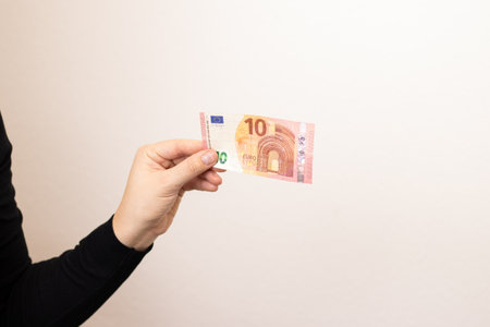 Close up of a woman holding one ten euro bill, grey backgroundの写真素材