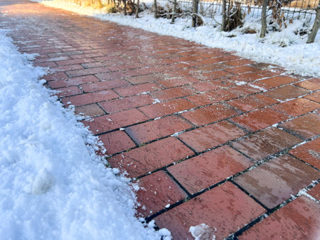 An icy pedestrian path sidewalk in winter with snow and sandの写真素材