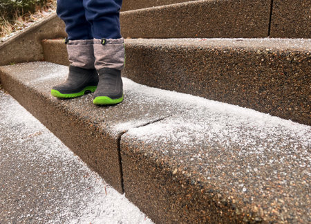 Close up of toddlers feet on stone steps outdoors covered with iced snow and salt