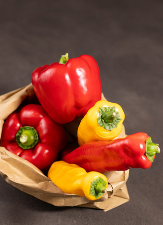 Close up of red bell pepper and pointed paprika in paper bag on grey table