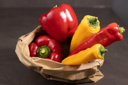 Close up of red bell pepper and pointed paprika in paper bag on grey tableの写真素材