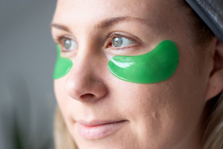 Close up of a caucasian millennial woman with no makeup and green gel moisturizing patches under her eyesの写真素材