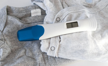 Close up of a digital positive pregnancy test on baby clothesの写真素材