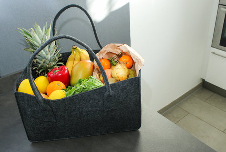 A grey eco felt bag on kitchen table with groceries, fresh vegetables and fruitsの写真素材