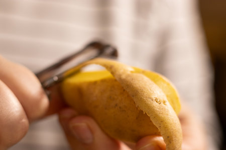 Close up of female hands peeling raw yellow potato, blurred backgroundの写真素材