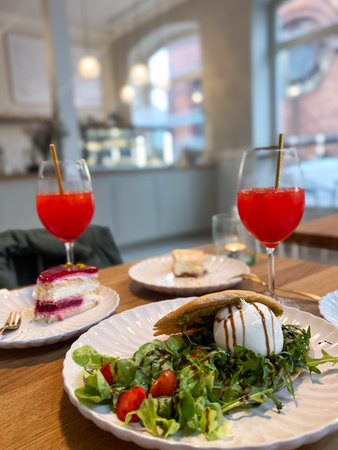 Cafe table with two orange cocktail drinks, two pieces of cake and a salad on a plateの写真素材