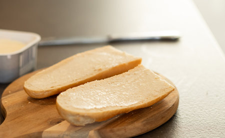 Close up of two slice of white baguette bread on wooden cutting board with butter