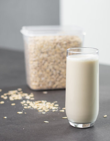 A glass of oat milk and oatmeal in a box on grey kitchen table. Vegan and non-dairy alternative milkの写真素材